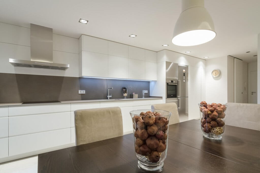 Cocina lineal en tonos blanco y beige con mesa de comedor en madera