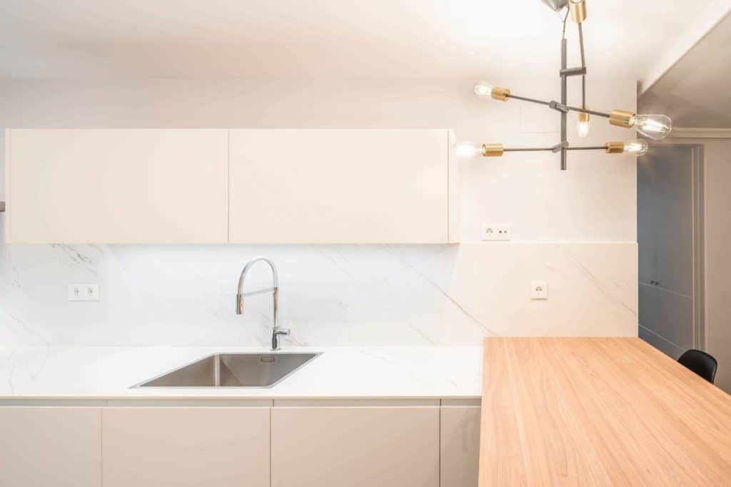 Cocina blanca con pequeña península en madera y lámpara de diseño