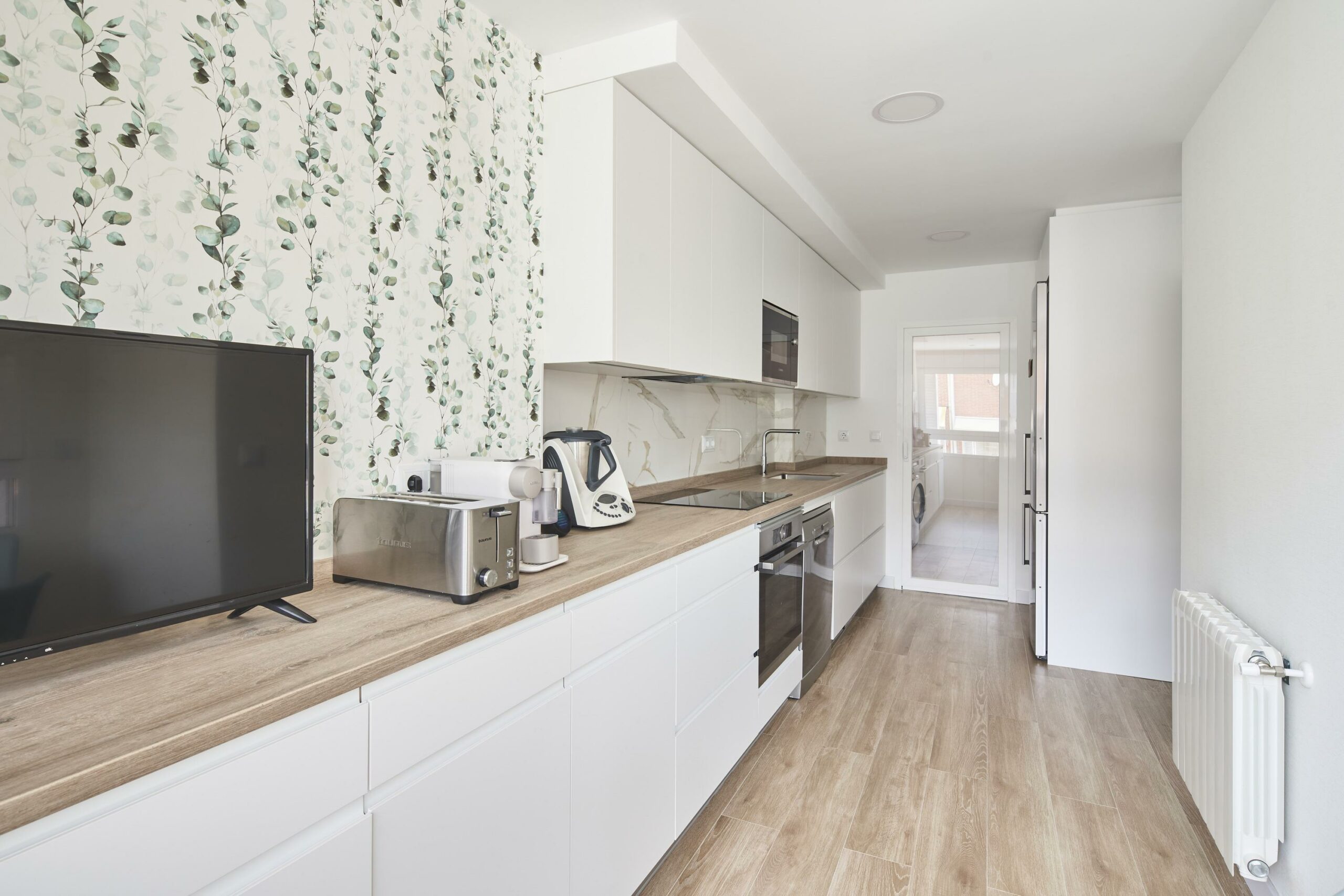 Cocina con el suelo y la encimera de madera y los acabados de los muebles en blanco