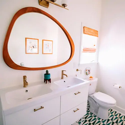 Cuaro de baño de color blanco con suelo con formas geométricas, Además tiene espejo de madera natural