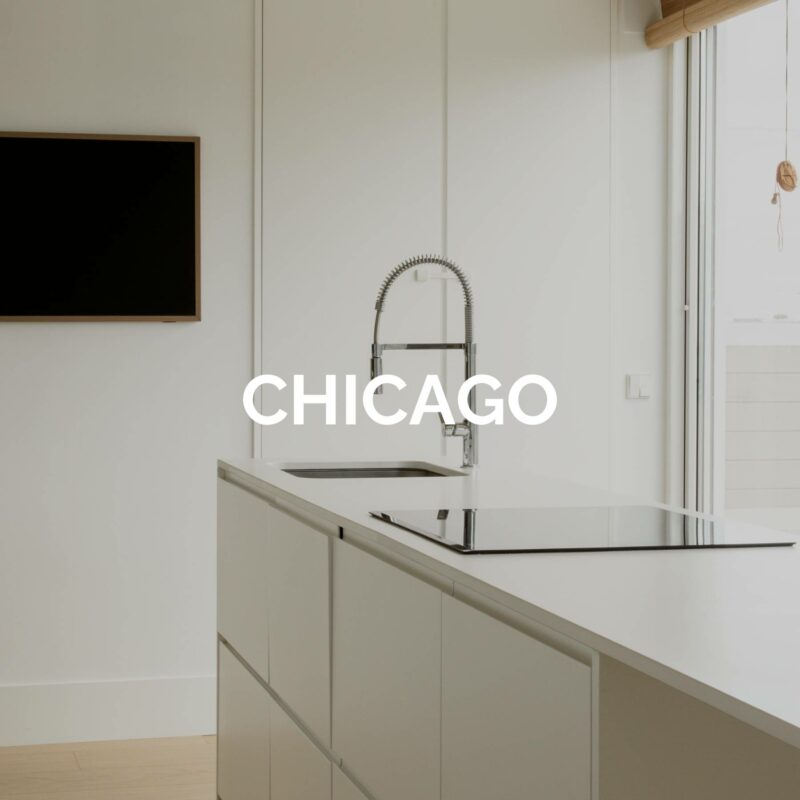 Cocina modelo Chicago en estilo minimalista Cocina minimalista con isla blanca, grifería profesional y el texto “CHICAGO” superpuesto en el centro.