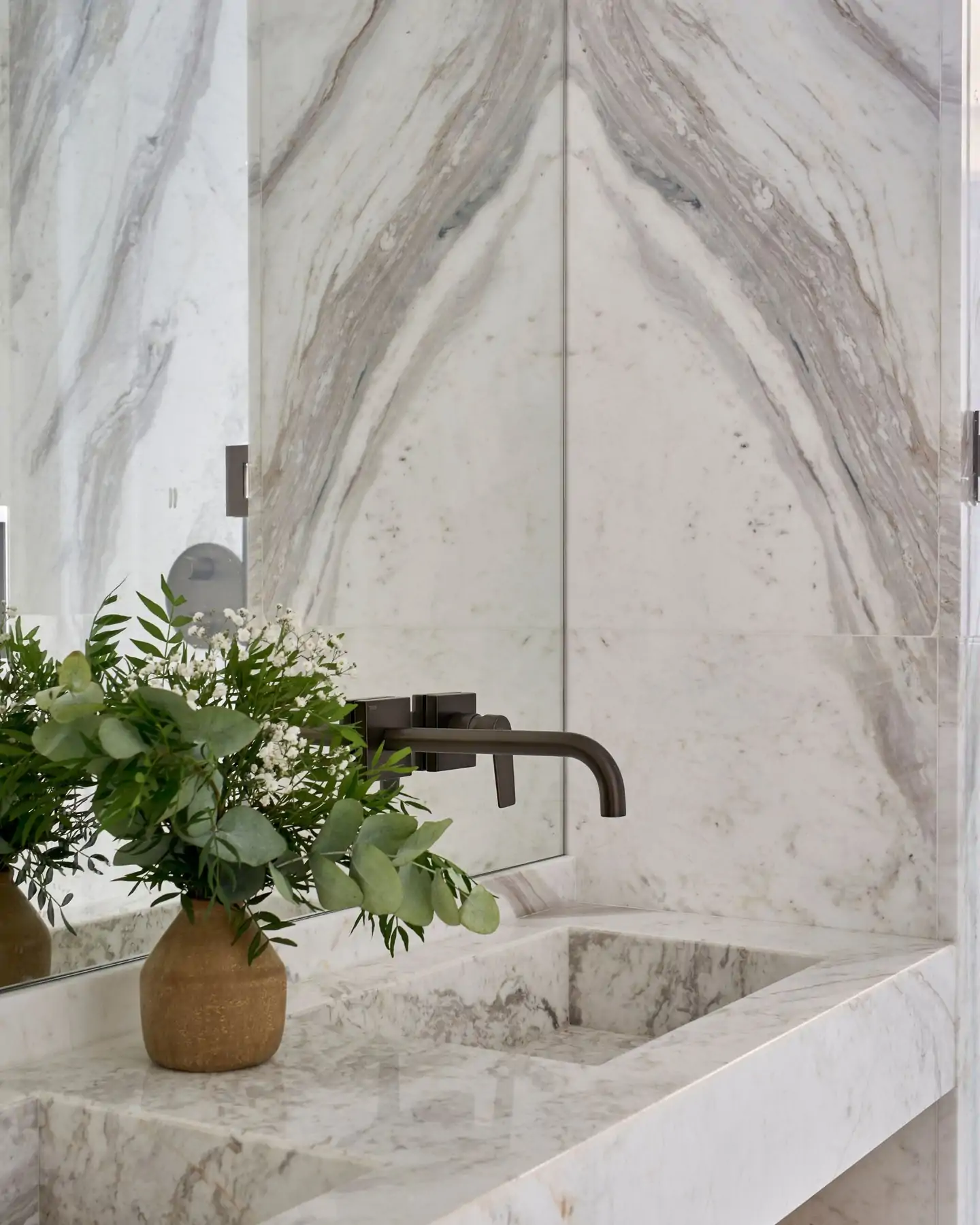 Lavabo de baño moderno en mármol – lujo y sofisticación en cada detalle. Lavabo de baño moderno en mármol blanco con grifería negra empotrada y jarrón decorativo.