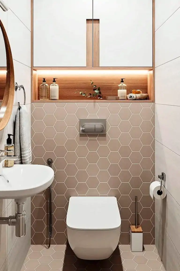 Baño compacto con revestimiento hexagonal beige, sanitario suspendido y hornacina retroiluminada en madera natural.