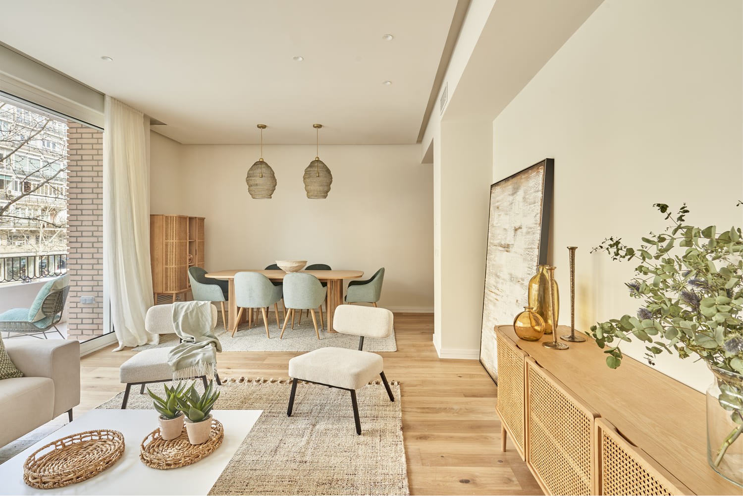 Salón-comedor luminoso con zona de estar en tonos neutros, mesa de comedor con sillas azules y decoración natural en madera y fibras.