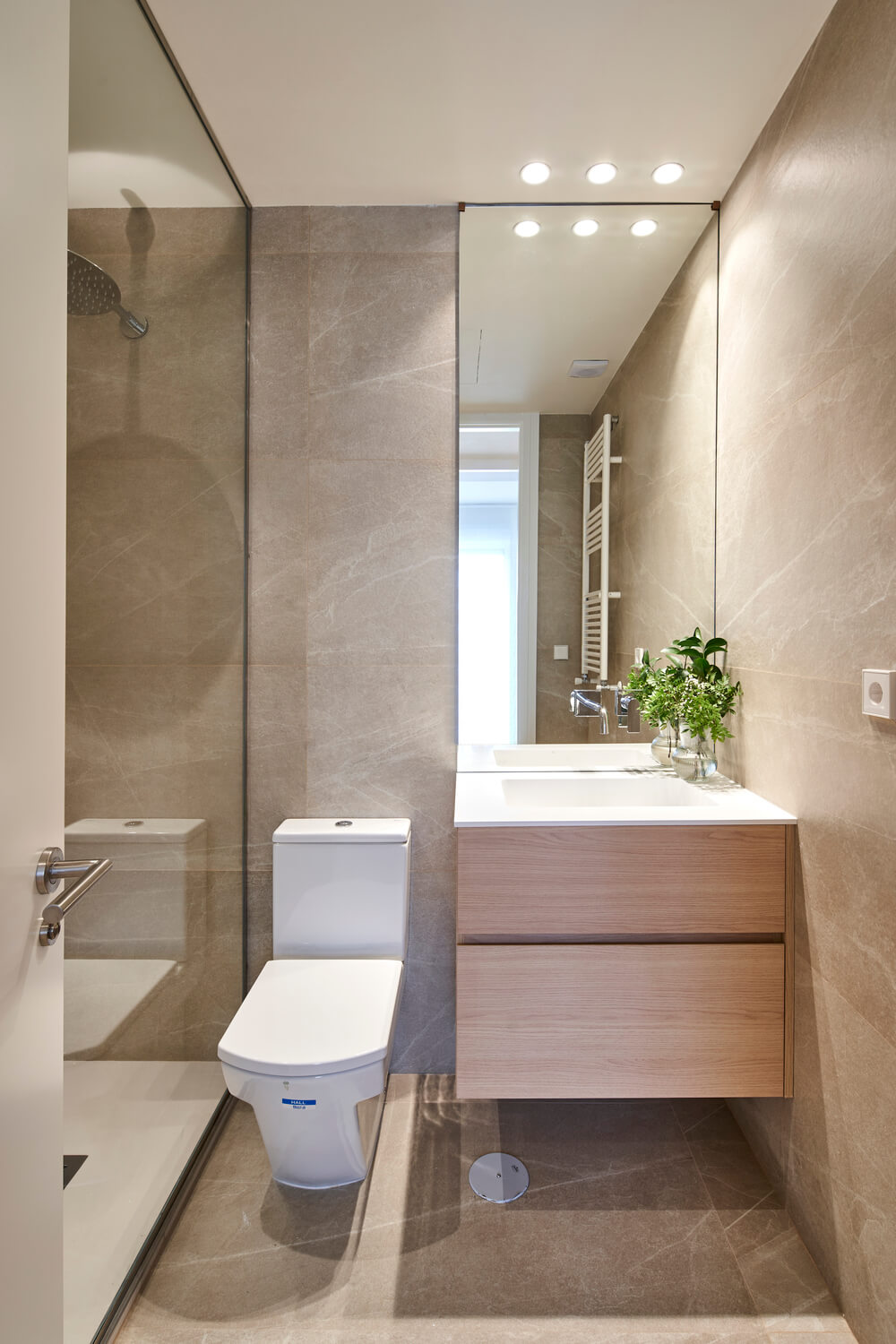 Baño contemporáneo en tonos beige con ducha acristalada Baño moderno en tonos beige con ducha acristalada, sanitario blanco y mueble de lavabo en madera clara.