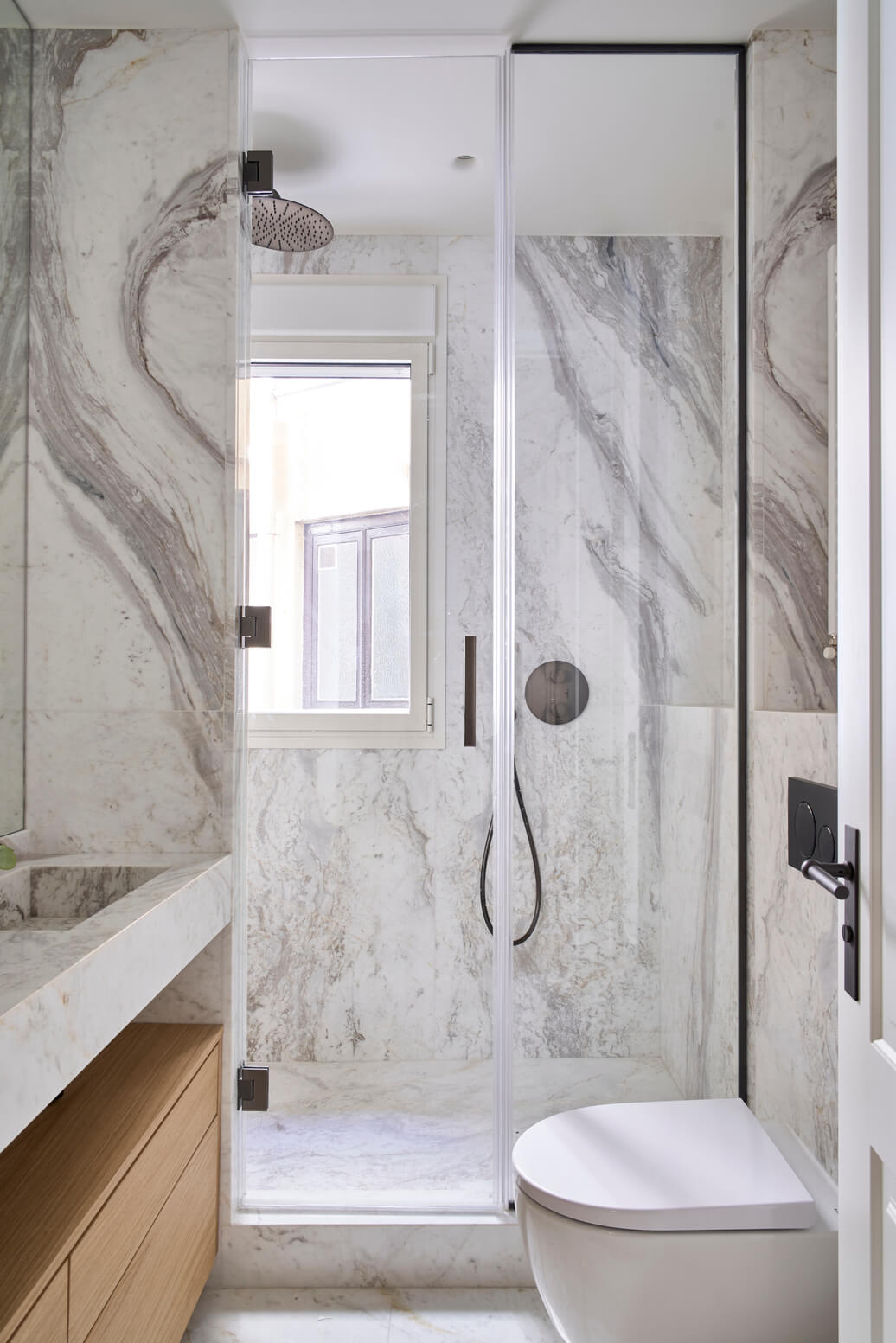 Baño en mármol con ducha acristalada y diseño minimalista Baño moderno en mármol claro con ducha acristalada, ventana y sanitario compacto en primer plano.