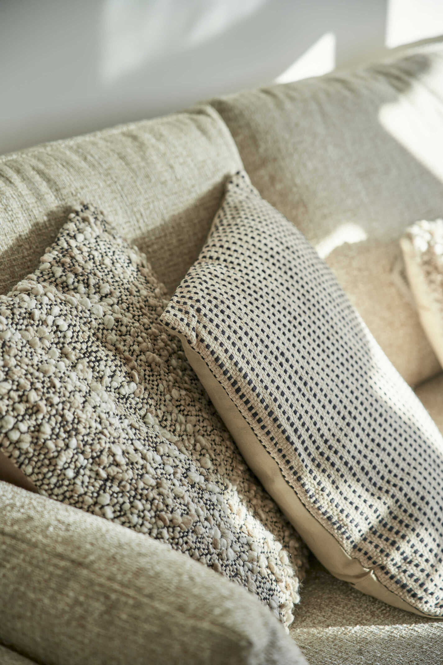 Cojines en tonos neutros con texturas artesanales sobre un sofá claro, creando un ambiente acogedor de estilo vintage.