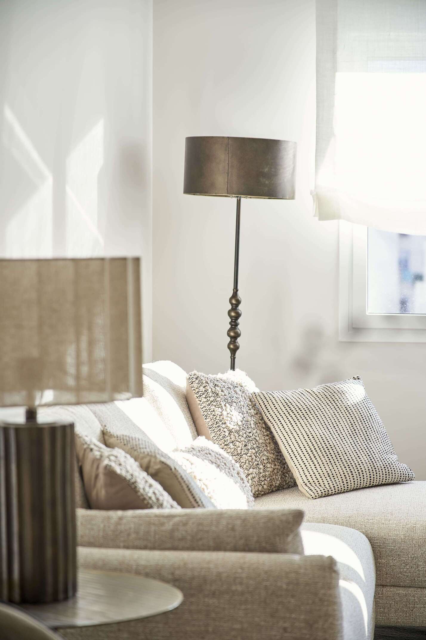 Rincón de salón de estilo vintage con sofá en tonos neutros, cojines tejidos y lámparas decorativas de inspiración retro.