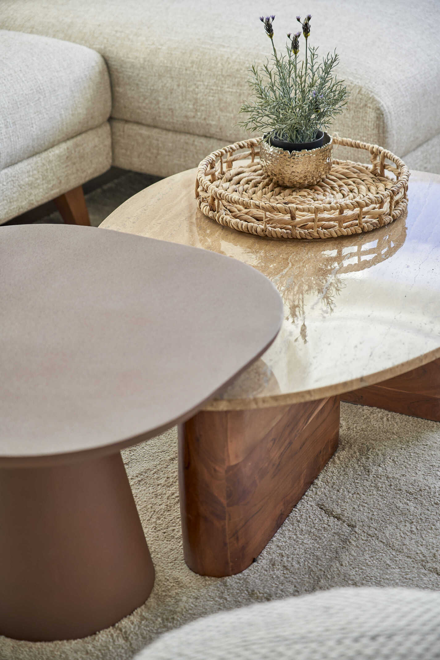 Mesa de centro con diseño orgánico en madera y mármol, decorada con bandeja de fibras naturales y planta, junto a sofá de textura bouclé.