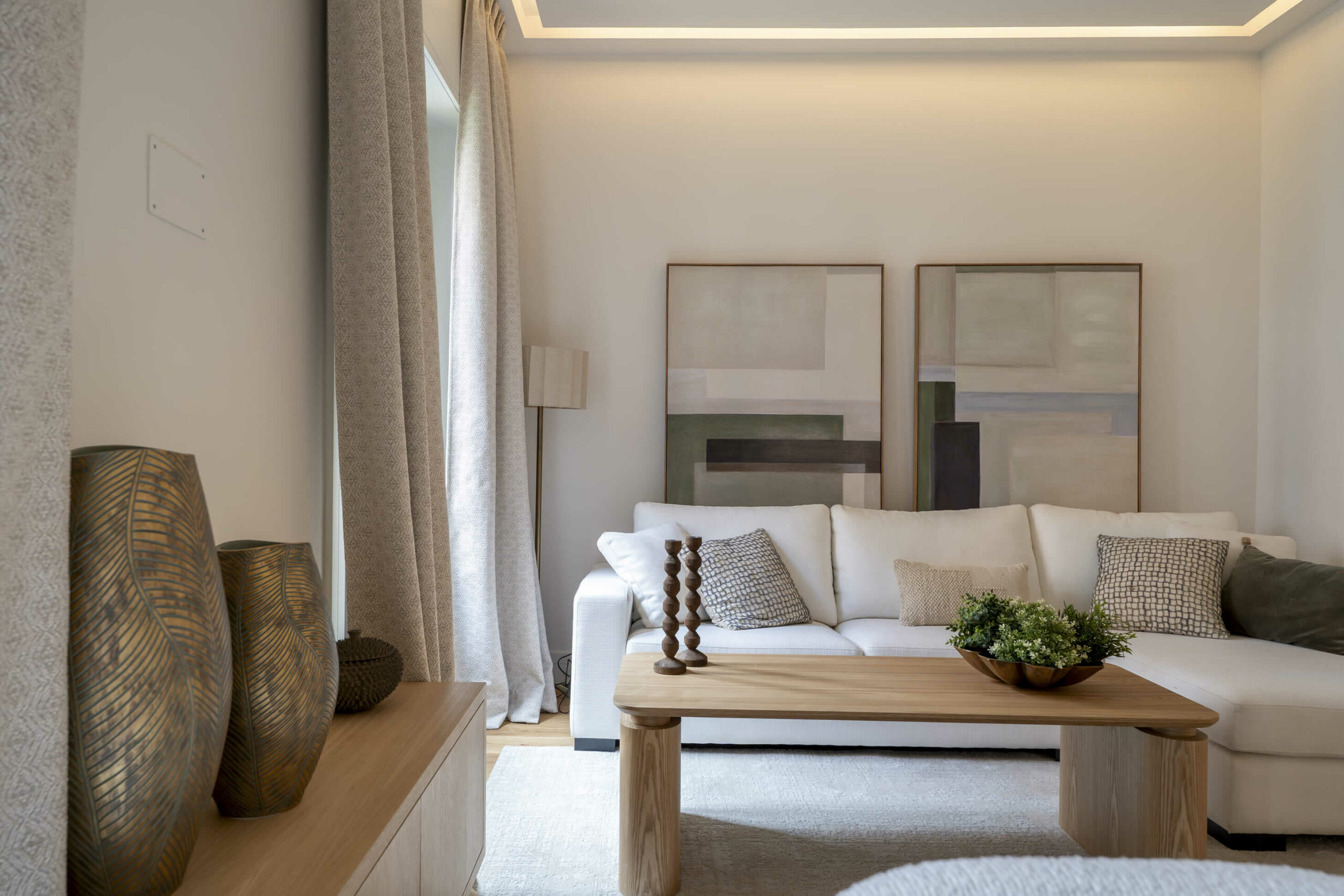 Salón moderno con sofá blanco, mesa de centro de madera, cuadros abstractos en tonos neutros y decoración en texturas naturales.